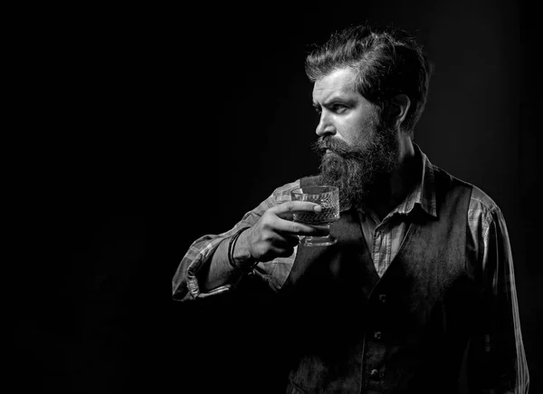 El hombre con barba sostiene un vaso de brandy. Bebida alcohólica de lujo. Hombre barbudo alegre está bebiendo whisky caro . — Foto de Stock