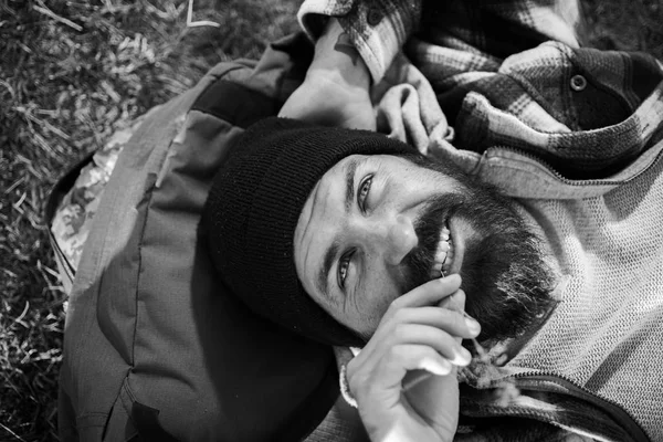 Vagabundo relaxante desfrutar do pôr do sol. Conceito de férias de verão. Homem barbudo hipster com barba longa paisagem verde natural. Turista relaxante jazia na mochila. Caminhadas de viajantes no dia ensolarado. Caminhante relaxante — Fotografia de Stock