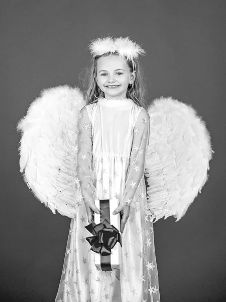 Angel child from heaven gives you gift. Cute toddler girl in white wings as Cupid. Angel kid with blonde curly hair. Happy little Angel. Wonderful blonde little girl in the image of an angel with