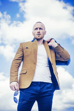 Takım elbiseli, güneş gözlüklü ve bulutlu gökyüzüne bakarken yüzünü çeviren yakışıklı genç adamın yakın çekimi. Bayım. Mükemmellik. Adam bulunmaya hazır. Yeni bir hayatın beklentisiyle.