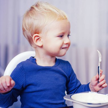 Çocuk sevimli bebek kahvaltı yiyor. Bebek beslenmesi. Sağlıklı yiyin. Toddler evde atıştırmalık yiyor. Çocuk lapa yer. Çocuk sevimli çocuk mavi gözleri tabak ve gıda ile masada oturup. Sağlıklı beslenme. Sağlıklı gıda