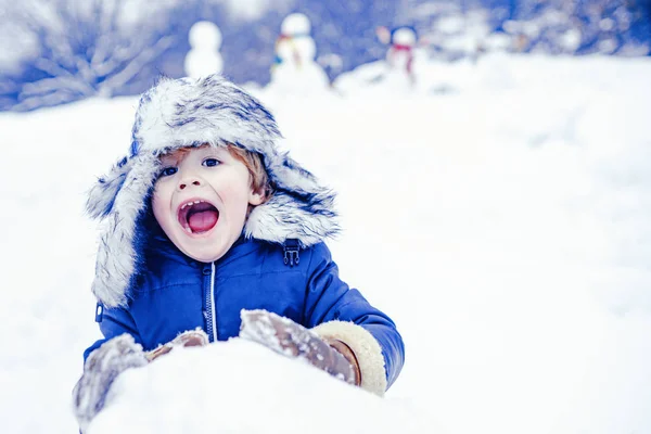 白い雪の背景に公園で雪と遊ぶ興奮した子供。寒い冬の公園の冬の子供たち。かわいい子供-冬の肖像画。雪の中で雪だるまと面白い男の子の子供. — ストック写真