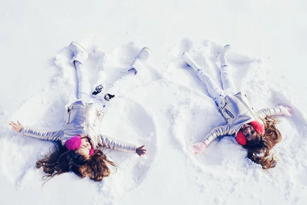 Two Girls on a snow angel shows. Smiling children lying on snow with copy space. Children playing and making a snow angel in the snow. Top view. — Stock Photo, Image