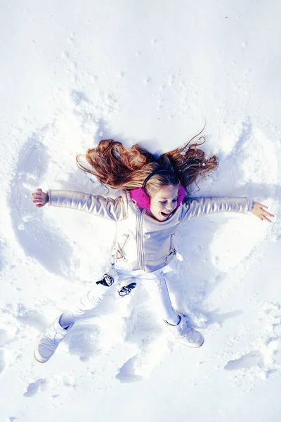 Улыбающийся ребенок лежит на снегу с копировальным пространством. Забавный ребенок делает снежного ангела. Девочка играет и делает снежного ангела в снегу . — стоковое фото