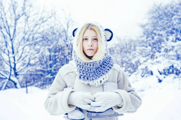 Giovane donna bionda in maglione e cappello divertente con pattini bianchi sulle spalle nella gelida giornata invernale. Vacanze invernali. Ragazza che gioca con la neve nel parco . — Foto Stock