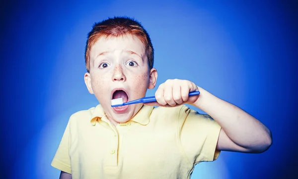 Child clean teeth with toothbrush. Kid with toothbrush isolated on blue background. Red-haired boy with funny face is brushing teeth with toothbrush. Happy child kid boy brushing teeth. — Stock Photo, Image