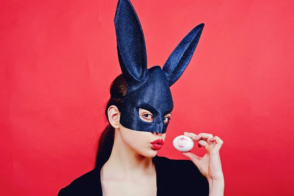 Pasen vrouw. Vrouw konijn, easter bunny meisje. Rode lip afdruk op easter egg op rode achtergrond. Vrouwelijke mond kus. Afdrukken van rode lippen op witte ei. — Stockfoto
