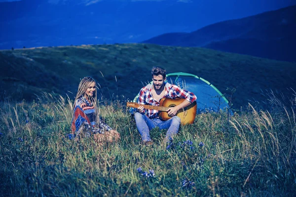 Increíble joven pareja amorosa en el campamento al aire libre en vacaciones alternativas libres acampar sobre las montañas. Viajeros felices descansando y tocando la guitarra. Estilo de vida activo y concepto de montañas increíbles . — Foto de Stock