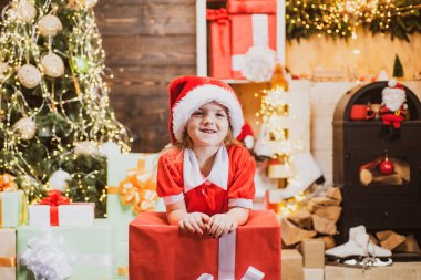 Çocuklar içeride Noel ağacının yanında eğleniyorlar. Mutlu çocuk iki eliyle kırmızı bir hediye kutusu tutuyor. Yeni yıl çocukları. Mutlu Noeller ve mutlu tatiller.