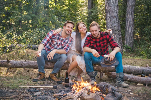 Ungdomar äter rostade marshmallows när de campar nära lägerelden. Vänners campingkoncept. Ungdomar som roar sig utomhus. — Stockfoto