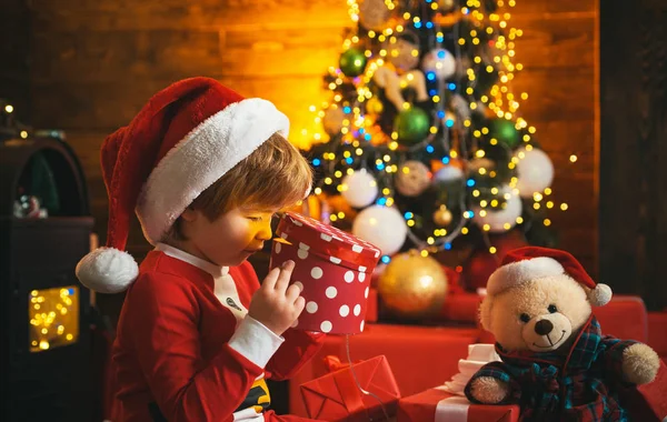 O miúdo feliz está a abrir uma caixa de presente. Tempo de Natal. Fundo da árvore de Natal. Conceito de férias . — Fotografia de Stock