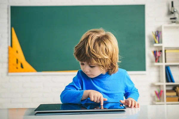 Escuela primaria y educación. Niño jugando con la tableta digital. Colegial con tablet digital en aula escolar . — Foto de Stock