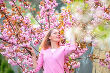 Sarışın kadın çiçek açan sakura bahçesinde bir anın tadını çıkarıyor. Güneşli bir bahar günü. Mutlu kız baharda çiçek açan ağaç bahçesinde vakit geçirir..
