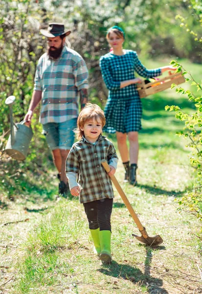 Keluarga bahagia: ibu, ayah, anak-anak dengan latar belakang kebun musim semi. Kehidupan petani keluarga di pedesaan. Keluarga petani yang ceria berdiri di kebun sayuran. Kehidupan desa . — Stok Foto