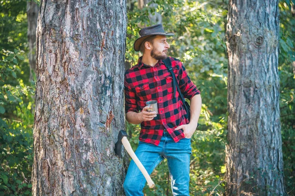 Vilar efter hårt arbete. Tema jordbruk och skogsbruk. Loggar. Olaglig avverkning fortsätter idag. Stilig ung man med yxa nära skogen. — Stockfoto