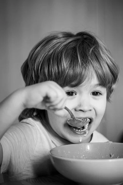 Cuidados infantis. Rapazinho a tomar o pequeno-almoço na cozinha. Comida e bebida para criança. Menino - ecologia Conceito de comida. Miúdo giro está comendo. Menino sentado na mesa e comendo lanche de leite . — Fotografia de Stock