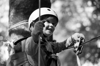 Eğitimli bir çocuk. Ağaç evdeki ya da halat parkındaki güvenlik ekipmanlarıyla tırmanan sevimli küçük çocuk ipe tırmanıyor. Güvenli tırmanış kaskla ekstrem spor