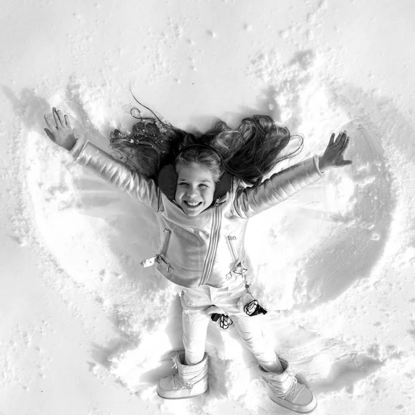 Funny kid making snow angel. Child girl playing and making a snow angel in the snow. Top view. — Stockfoto