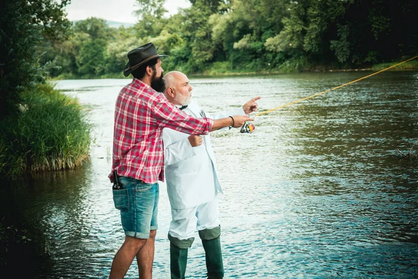 Bearded man and elegant businessman fishing together. Two fishermen relaxing together with beer while fishing on the lake at the morning. Man relaxing and fishing by lakeside. Stock Photo