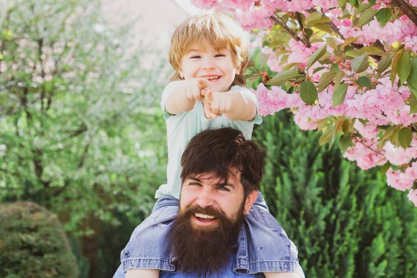 Ritratto di padre felice che fa cavalcare il figlio sulle spalle e alza lo sguardo. Padre con figlio che si diverte in parco. Giorno di padri . — Foto Stock