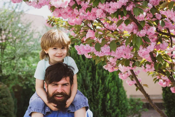 Buon padre che fa un giro in spalla sulle spalle in giardino. Un bel bambino che abbraccia suo padre. Padre e figlio si rilassano insieme. Giorno di padri . — Foto Stock