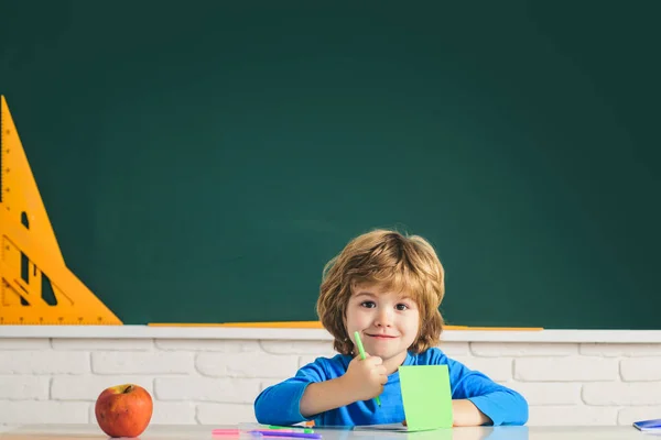 Funny child from elementary school. Children learning. Cute child boy in classroom near blackboard desk. Chalkboard copy space.