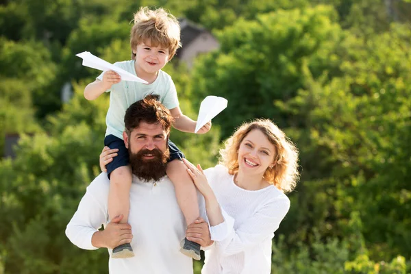 Glücklicher Vater beim Schulterzucken. Glückliches Kind zeigt seinen Eltern Papierflugzeug. Glückliche Familie und kleiner Sohn spielen am blauen Sommerhimmel. Gartenparty in Amerika. — Stockfoto