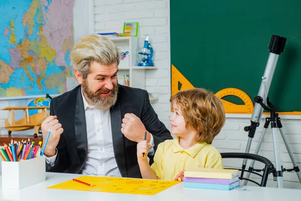 Elementary school tutor. Preschool education. Cute child boy with teacher in classroom near blackboard desk.