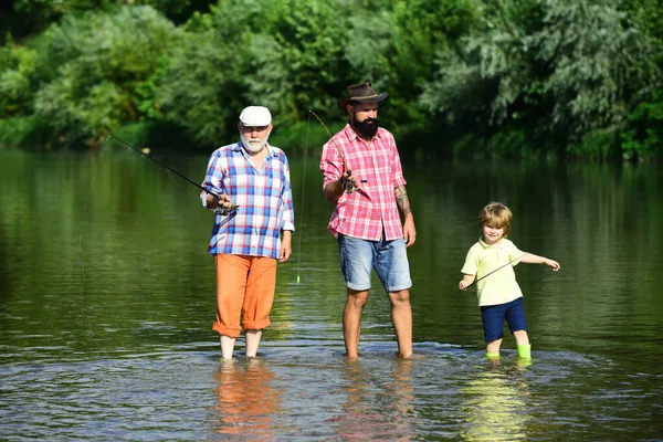 Nonno, padre e figlio pescano a mosca sul fiume. Un legame familiare. Giornata estiva. Un uomo che insegna ai bambini a pescare nel fiume. Buon pescatore con canna da pesca. Vecchi e giovani . — Foto Stock