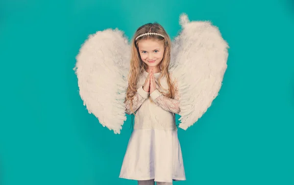 Valentines Day. Angels little hands crossed for you. Mischievous little angel girl standing with your clenched fists. Beautiful little angel girl standing with your arms close to your chest as in Stock Photo