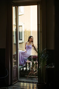 Güzel genç bir kadın balkonda sabahın tazeliğinin tadını çıkarıyor. Şeffaf gecelikli kadınlar. Güzel kız tazeliğin tadını çıkarıyor. Ev manzaralı balkon.