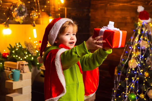 Menino feliz perto da árvore de Natal dando a alguém um presente de Natal. O miúdo está a usar roupa de Pai Natal. Conceito de Natal . — Fotografia de Stock