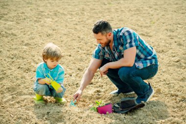 Baba oğluna bahçecilik öğretiyor. Çiftçi ailesi bahçede sebze topluyor. Aile birlikte çalışıyor. Aile bahçesinde çalışırken baba ve oğulun portresi.