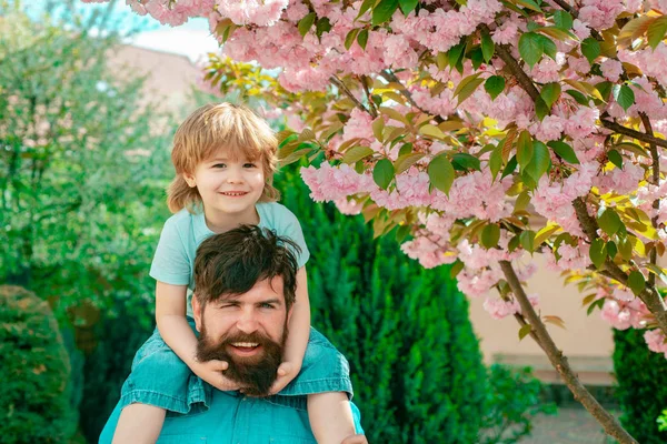 Padre e figlio si rilassano insieme. Buon padre che fa un giro in spalla sulle spalle in giardino. Felice giorno dei padri . — Foto Stock