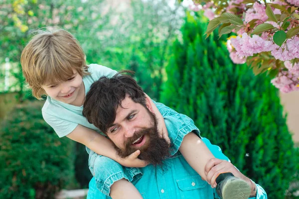 Happy fathers day. Happy father giving shoulder ride on his shoulders in garden. Father and son relaxing together. — Stock Photo, Image