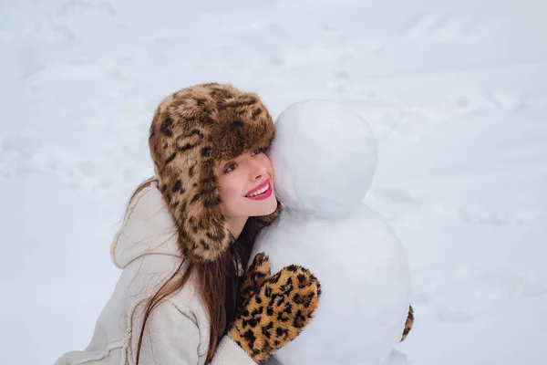 Boneco de neve e garota engraçada o amigo está de pé em chapéu de inverno e cachecol com nariz vermelho. Boneco de neve e garota engraçada na neve. Menina brincando com boneco de neve - isolado no fundo da neve . — Fotografia de Stock