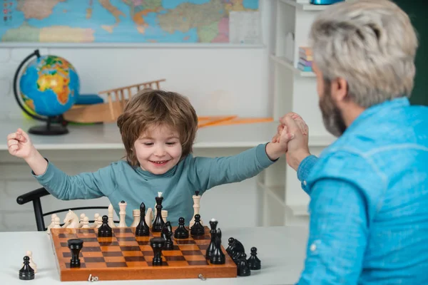 Jonge jongen die schaak speelt met vader en plezier heeft. Educatieve spelletjes. Knappe vader en zoon spelen schaak terwijl ze samen tijd doorbrengen.. — Stockfoto