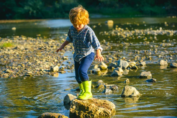 Ребенок на озере или реке. Ребенок проходит через реку. Прогулка в парке в солнечный весенний день. Мальчик смотрит на воду . — стоковое фото