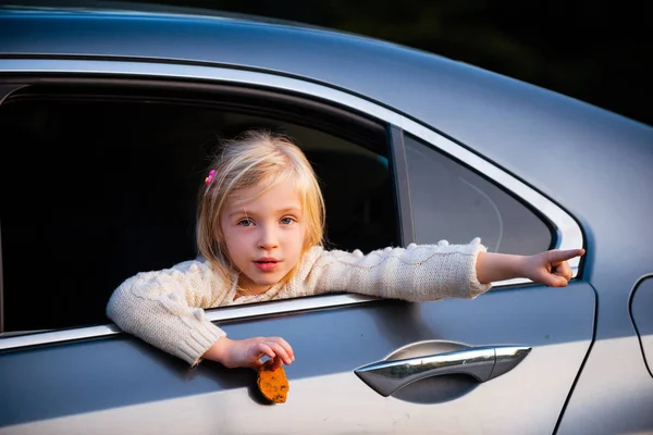 Bambina guarda fuori dal finestrino in macchina e qualcosa mostra una mano . — Foto Stock