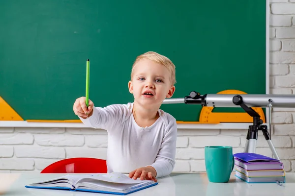 Śmieszne korepetycje ucznia. Przyjazne dziecko w klasie przy biurku z tablicą. Dzieciak uczy się w klasie na tle tablicy.. — Zdjęcie stockowe