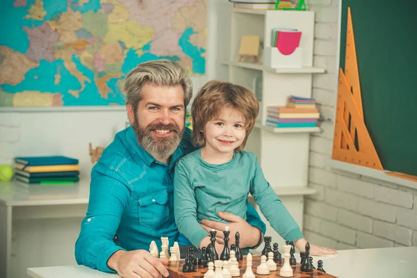 Učitel a školák hrají šachy ve třídě. Šťastné dvě generace mužů se baví a hrají šachy. Otec a syn. — Stock fotografie