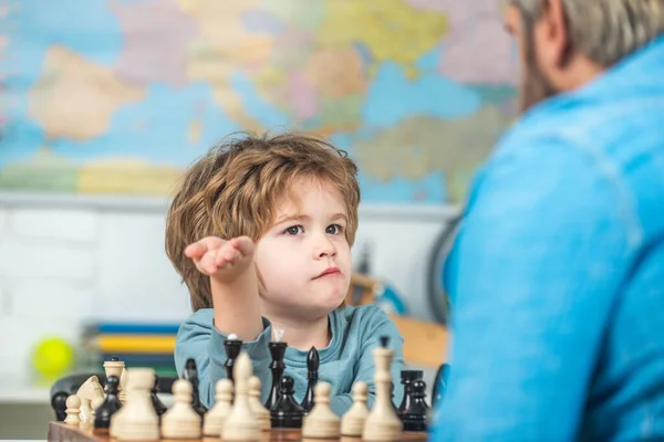 Zoon speelt thuis schaak met vader. Kleine slimme jongen die aan schaken denkt. Thuis tutor helpen jongen met studies schaken. — Stockfoto