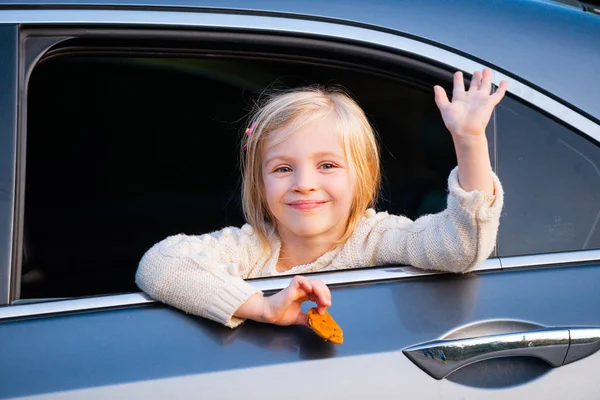 Una ragazzina sta mettendo la testa fuori dal finestrino dell'auto. Viaggio o concetto di viaggio. I bambini felici viaggiano in macchina. Carino bambino appoggiato fuori dalla finestra di un furgone, sorridente e agitando . — Foto Stock