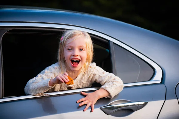 Heyecanlı küçük kız caddedeki arabaya hayran bakıyor. Gülümseyen ve arabasıyla seyahat eden şirin bir kız çocuğu.. — Stok fotoğraf