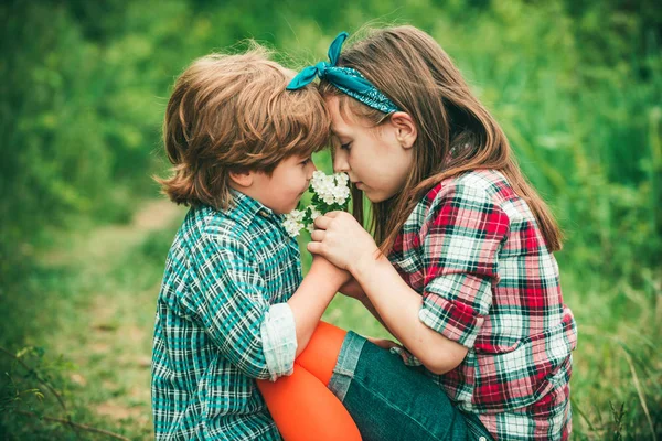 Niños sentados en un prado soplando flores de diente de león siendo felices y juguetones. Niño y niña soplando diente de león . — Foto de Stock