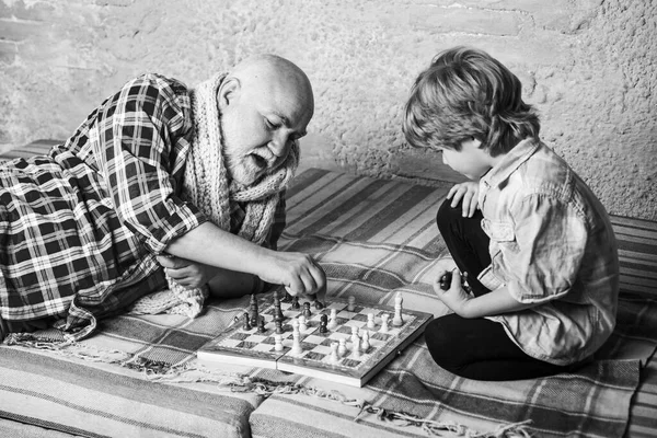 Senior man funderar på sitt nästa drag i ett parti schack. En liten pojke som spelar schack med sin farfar. Schack. Barndom. — Stockfoto