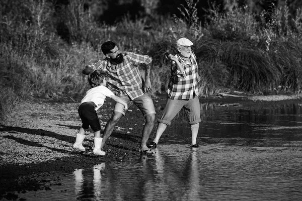 Male Child with Father and Grandfather Skipping Stones on Water. Man in different ages.