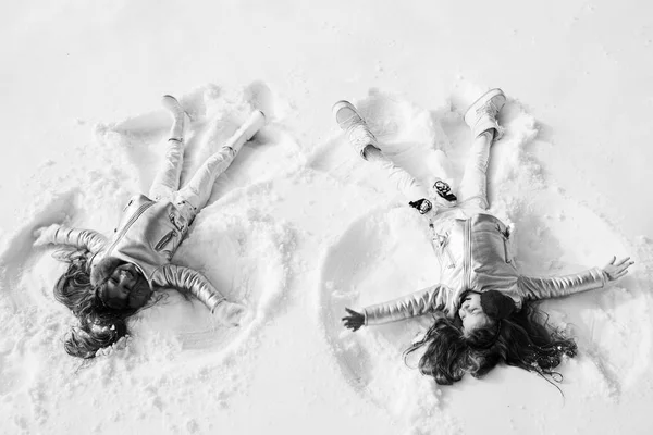 Dwie dziewczyny w śnieżnym aniele. Uśmiechnięte dzieci leżące na śniegu z przestrzenią do kopiowania. Dzieci bawią się i robią śnieżnego anioła w śniegu. Widok z góry. — Zdjęcie stockowe