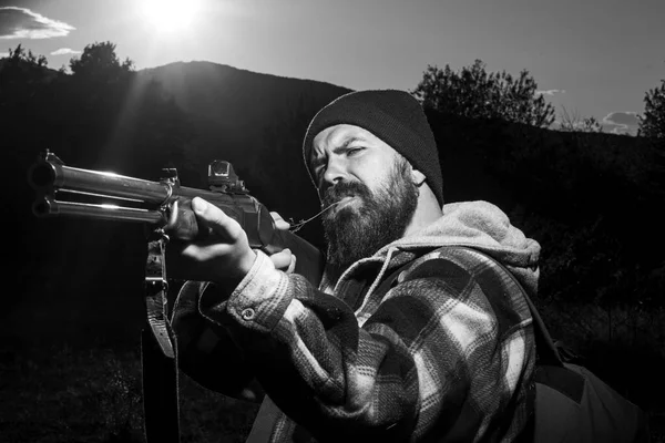 Szakállas vadász ember tartja a fegyvert, és séta erdőben. Puska-vadász rajzolódott ki, a gyönyörű naplemente. Autunm vadászat. Hegyi vadászat. Hordó egy pisztoly. — Stock Fotó