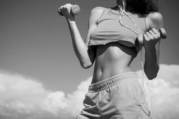 Cintura fina. Mulher a treinar com halteres no fundo do céu. Cintura de fitness. Abdominais fortes mostrando . — Fotografia de Stock